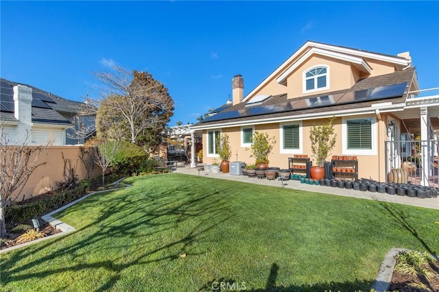 rear view of property featuring solar panels, fence, a lawn, and stucco siding