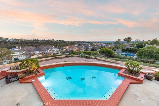 pool at dusk featuring an outdoor pool, a patio, and fence