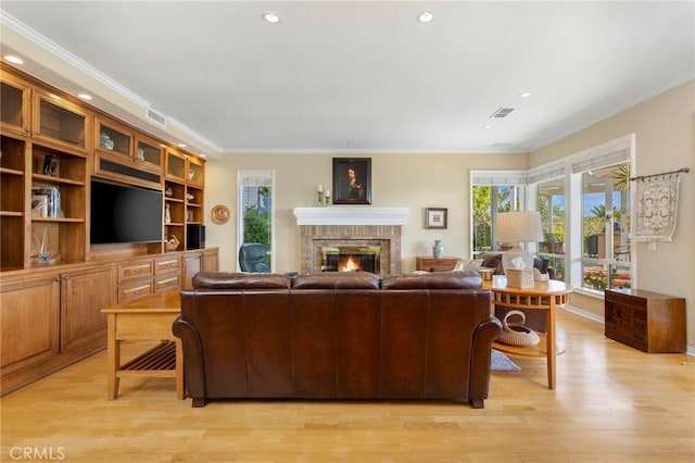 living area with light wood-type flooring, ornamental molding, a brick fireplace, and visible vents