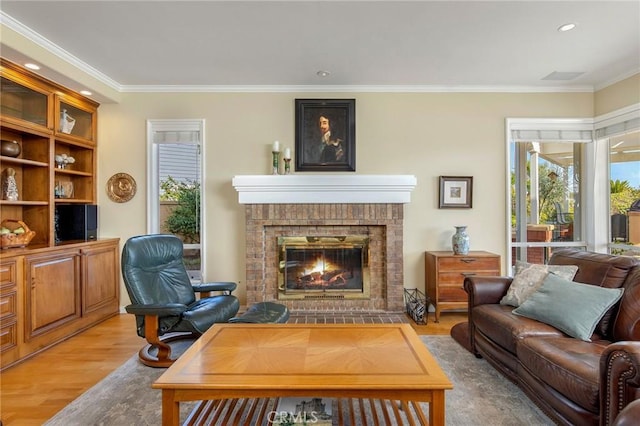 living area featuring ornamental molding, a brick fireplace, light wood-type flooring, and a healthy amount of sunlight