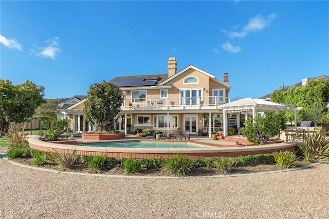 rear view of property with an outdoor pool, a patio, a balcony, french doors, and a pergola