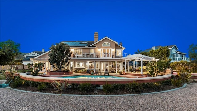 back of house with a fenced in pool, a patio, a chimney, roof mounted solar panels, and a balcony