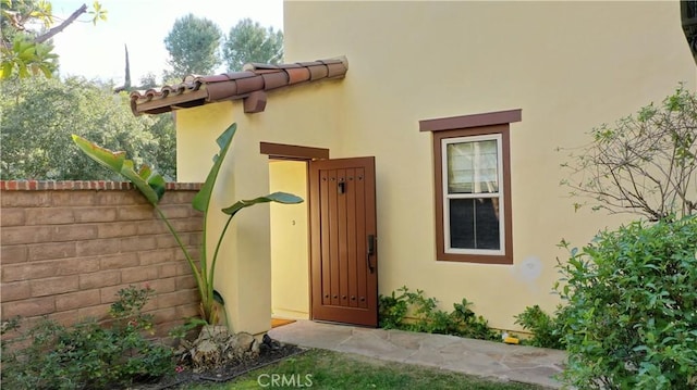 property entrance featuring stucco siding, fence, and a tiled roof