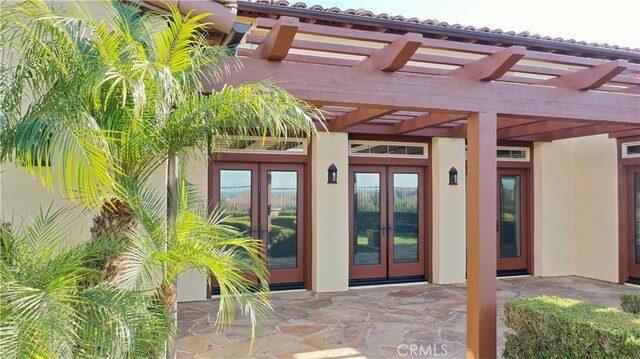 view of exterior entry featuring stucco siding, a patio area, a pergola, and french doors