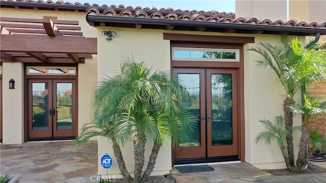 view of exterior entry with stucco siding, a tiled roof, a pergola, and french doors