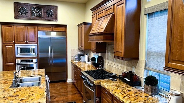 kitchen featuring built in appliances, dark wood-style flooring, a sink, tasteful backsplash, and custom range hood