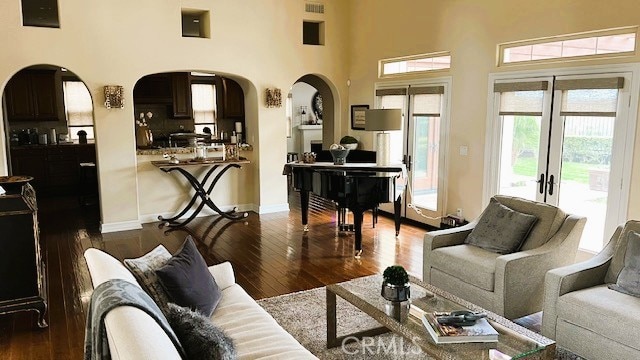 living room featuring baseboards, a high ceiling, arched walkways, and dark wood finished floors