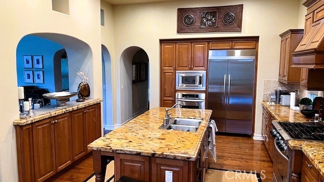 kitchen featuring dark wood-style floors, built in appliances, a kitchen island with sink, custom exhaust hood, and a sink