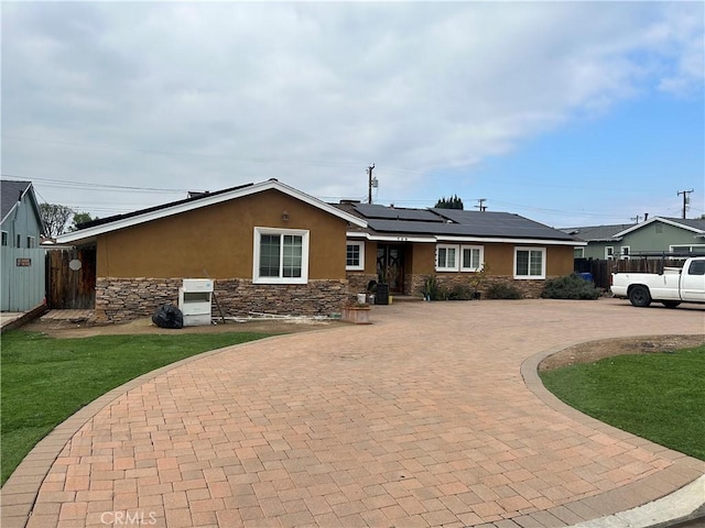 ranch-style home with solar panels, stone siding, fence, decorative driveway, and stucco siding