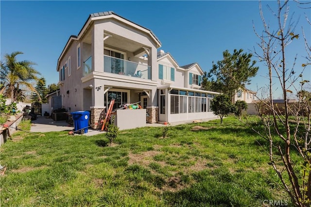 back of house with stucco siding, a lawn, a balcony, and a sunroom