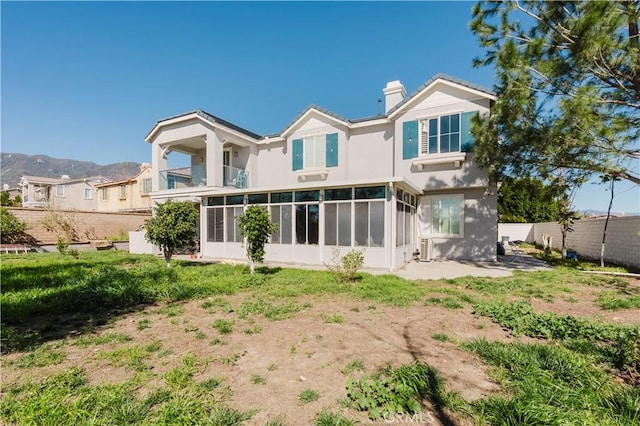 rear view of property featuring a balcony, a sunroom, a chimney, fence, and stucco siding