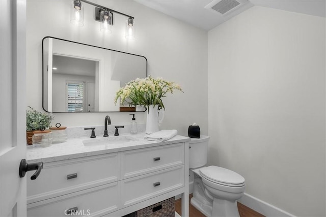 bathroom featuring toilet, vanity, visible vents, and baseboards