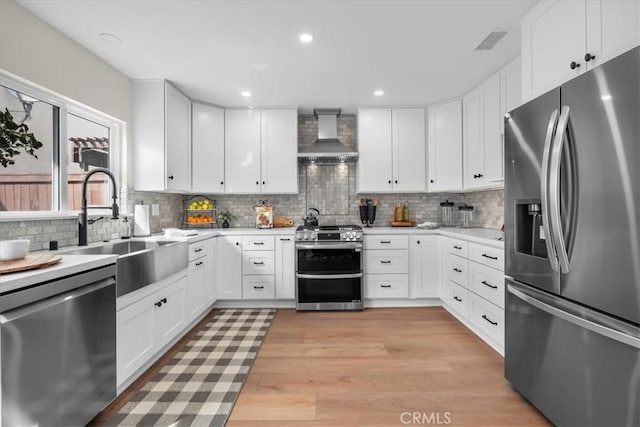 kitchen featuring light wood-style flooring, a sink, visible vents, appliances with stainless steel finishes, and wall chimney range hood