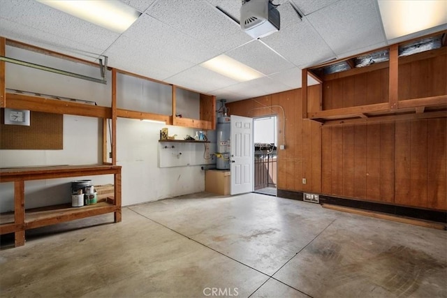 garage with strapped water heater, wood walls, and a garage door opener