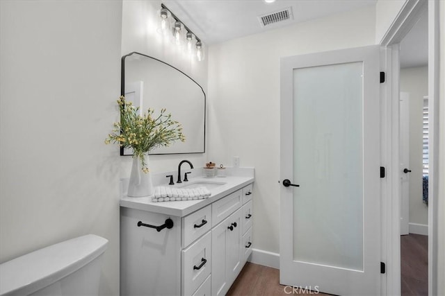 half bathroom with visible vents, toilet, vanity, wood finished floors, and baseboards