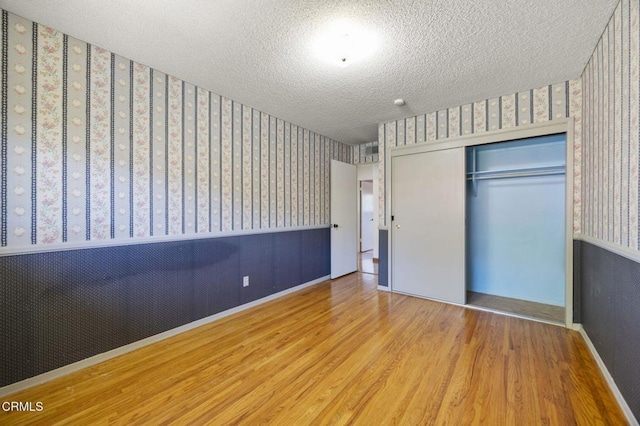 205 Bluefield Ave, Newbury Park, CA 91320 - unfurnished bedroom with wallpapered walls, wood finished floors, a closet, a textured ceiling, and a wainscoted wall
