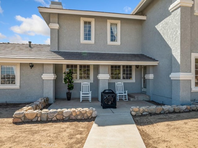 property entrance with a chimney, a tile roof, and stucco siding