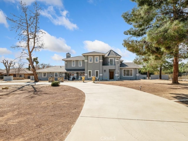 prairie-style home with a chimney, stucco siding, fence, a balcony, and driveway