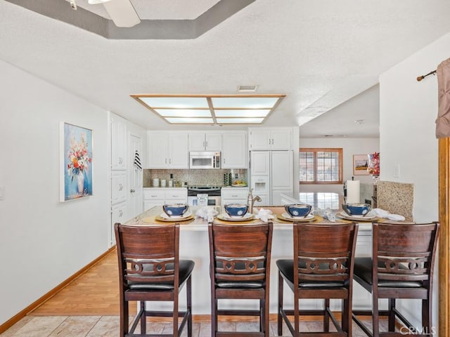 kitchen with a breakfast bar area, tasteful backsplash, appliances with stainless steel finishes, white cabinetry, and a peninsula