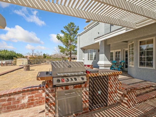 view of patio with exterior kitchen, grilling area, fence, and a pergola