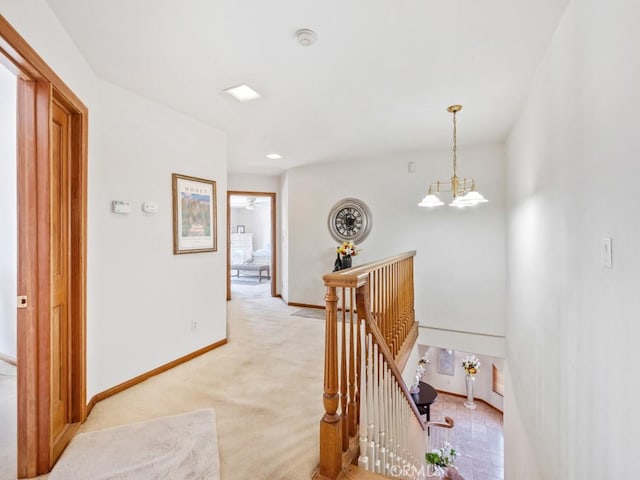 hall with baseboards, light colored carpet, a notable chandelier, and an upstairs landing