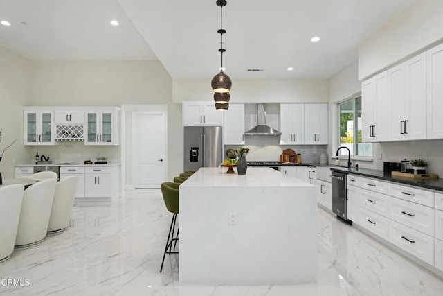 kitchen featuring wall chimney range hood, a breakfast bar area, white cabinets, stainless steel refrigerator with ice dispenser, and marble finish floor