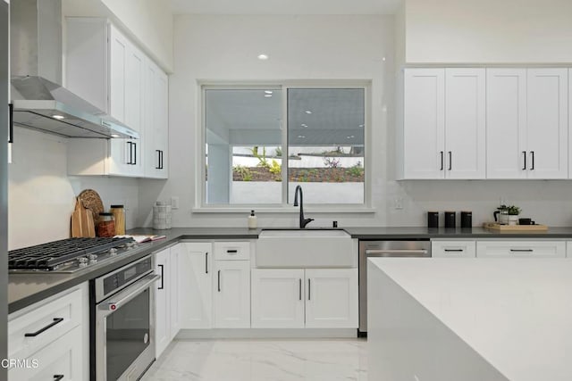 kitchen with marble finish floor, a sink, white cabinetry, stainless steel appliances, and wall chimney range hood