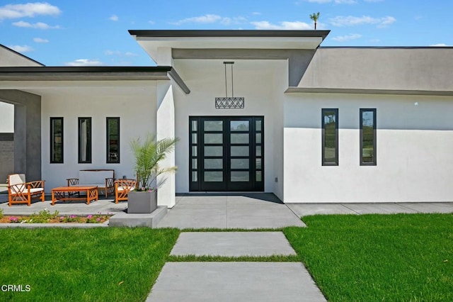 property entrance featuring stucco siding, a patio, and a yard