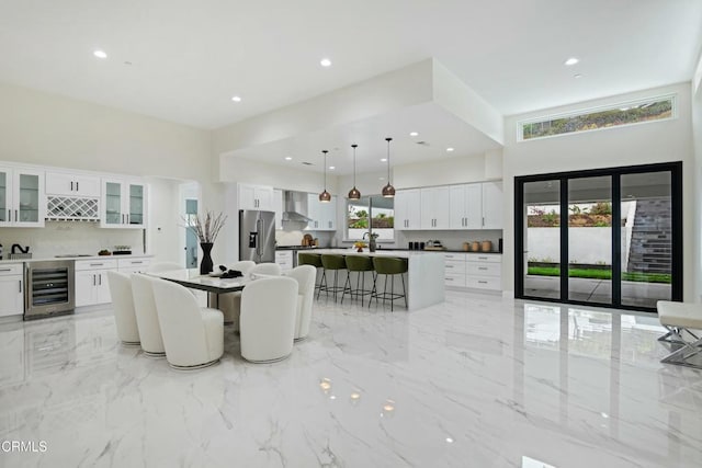 kitchen with a kitchen island, wall chimney range hood, wine cooler, a kitchen breakfast bar, and stainless steel fridge