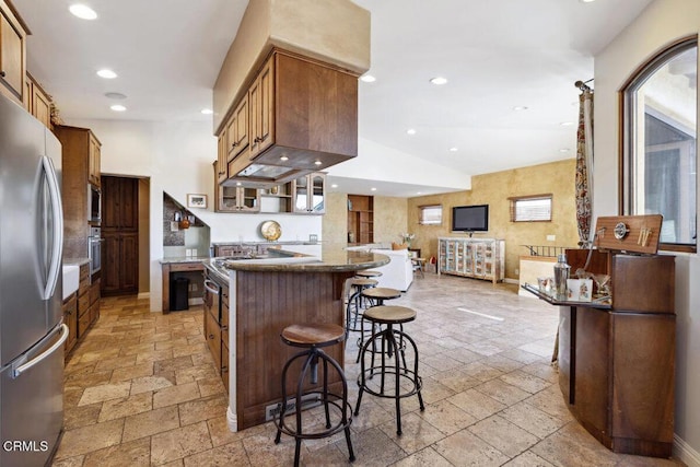 kitchen with appliances with stainless steel finishes, recessed lighting, stone tile flooring, and a breakfast bar area