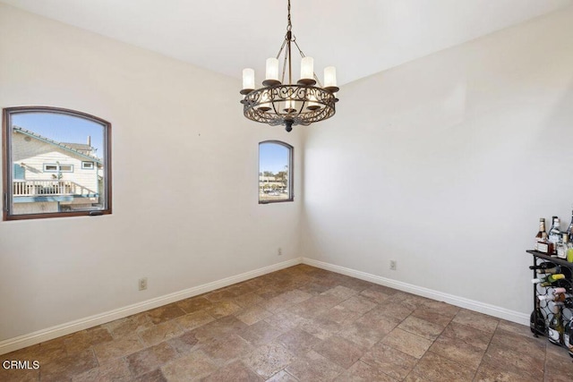 unfurnished room featuring stone finish floor, an inviting chandelier, and baseboards