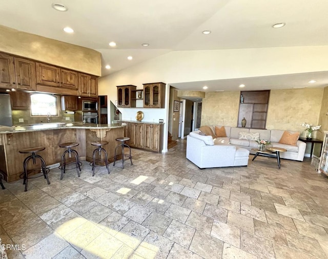 kitchen featuring lofted ceiling, appliances with stainless steel finishes, stone finish flooring, a kitchen bar, and glass insert cabinets