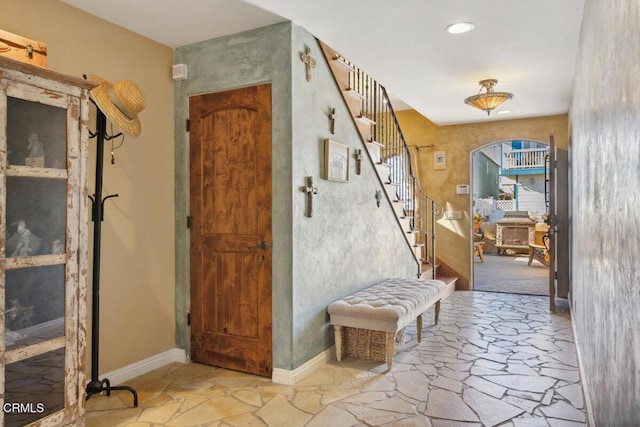 entryway featuring arched walkways, stone tile flooring, stairway, and baseboards