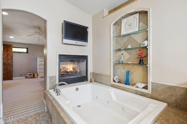 bathroom featuring a tub with jets, a glass covered fireplace, a ceiling fan, and recessed lighting