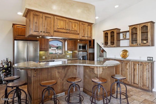 kitchen with tasteful backsplash, stone tile flooring, appliances with stainless steel finishes, glass insert cabinets, and a sink