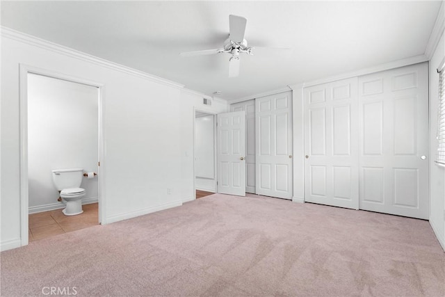 unfurnished bedroom with baseboards, connected bathroom, ornamental molding, carpet flooring, and two closets