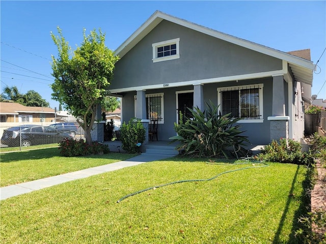 bungalow-style home with covered porch, fence, a front lawn, and stucco siding