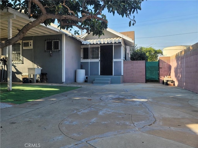 view of front facade featuring entry steps, a patio, a wall unit AC, fence, and stucco siding