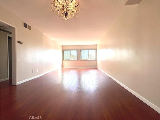 empty room with baseboards, dark wood-type flooring, visible vents, and an inviting chandelier