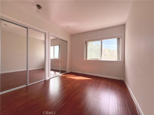 unfurnished bedroom featuring wood finished floors, baseboards, and two closets