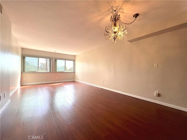 unfurnished room with dark wood-style flooring, visible vents, a notable chandelier, and baseboards