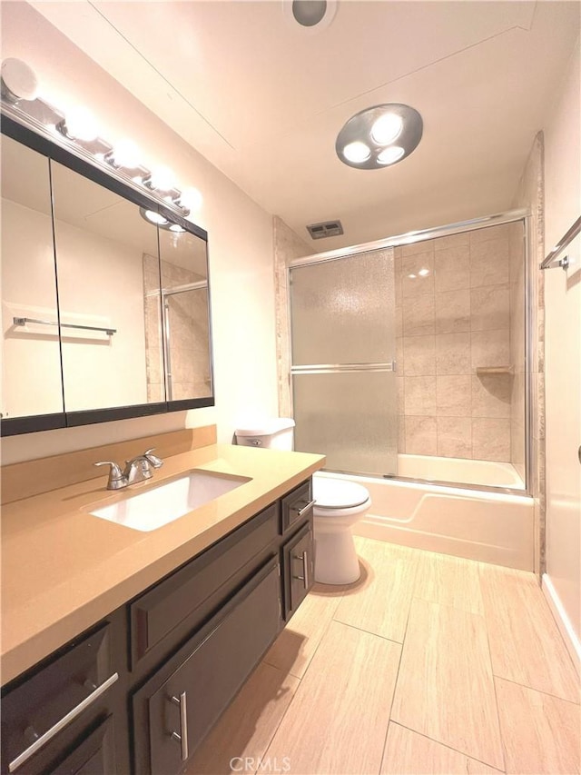 bathroom with toilet, bath / shower combo with glass door, vanity, and visible vents