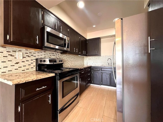 kitchen with recessed lighting, stainless steel appliances, dark brown cabinets, backsplash, and light stone countertops