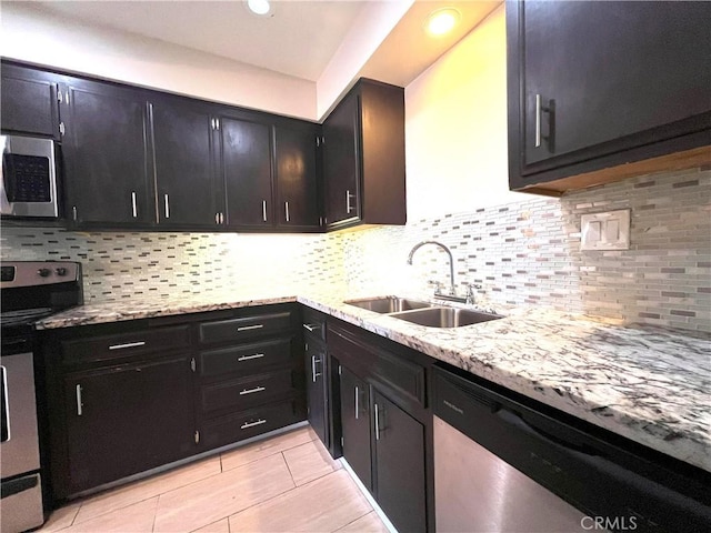 kitchen with light stone counters, dark cabinets, a sink, appliances with stainless steel finishes, and tasteful backsplash