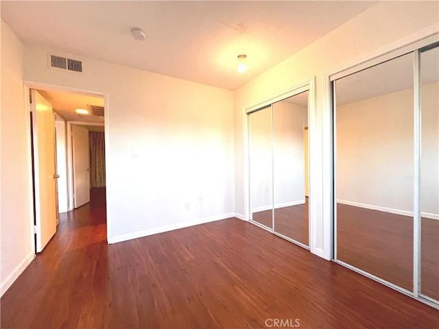 unfurnished bedroom featuring dark wood-style flooring, two closets, visible vents, and baseboards