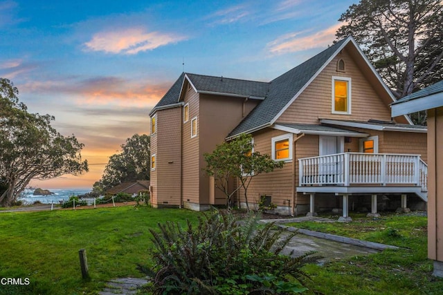 back of property at dusk featuring roof with shingles, a lawn, and a wooden deck