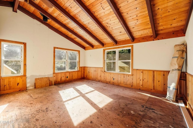 empty room with a wealth of natural light, wooden ceiling, a wainscoted wall, and vaulted ceiling with beams