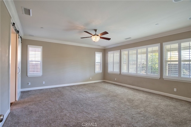 carpeted spare room featuring a wealth of natural light, visible vents, crown molding, and a barn door