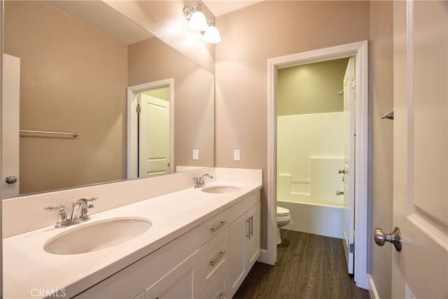 bathroom with toilet, double vanity, a sink, and wood finished floors