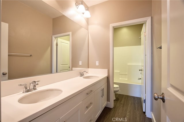 bathroom featuring double vanity, toilet, a sink, and wood finished floors